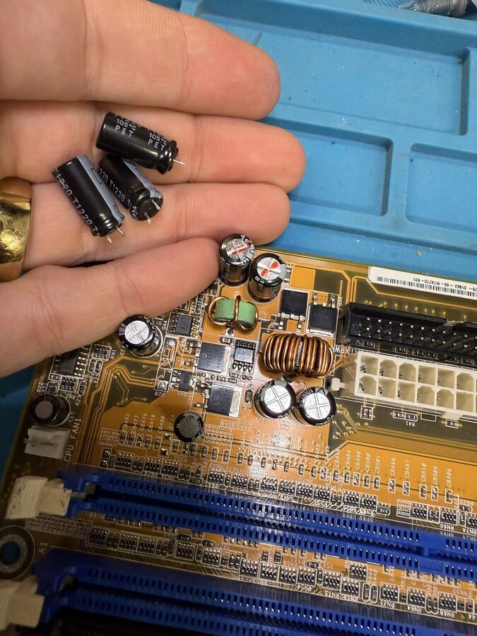 Swollen capacitors held in a hand above the board they came off